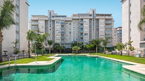 A swimming pool surrounded by a well-maintained lawn and palm trees, with modern apartment buildings in the background. - RELAX BY THE SEA, POOL, WIFI A / C. (Rincón de la Victoria)