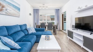 A modern living room with a blue sofa, a white coffee table, and a flat-screen TV. - RELAX BY THE SEA, POOL, WIFI A / C. (Rincón de la Victoria)