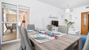 A dining area with a wooden table set for four, white walls, a television, and a door. - RELAX BY THE SEA, POOL, WIFI A / C. (Rincón de la Victoria)