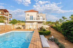 Un edificio de dos pisos con piscina, terraza de madera y jardín.
