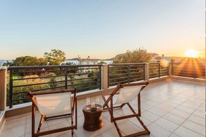 Un balcón con dos sillas de madera y una pequeña mesa redonda, con vistas a un paisaje pintoresco con edificios y árboles.