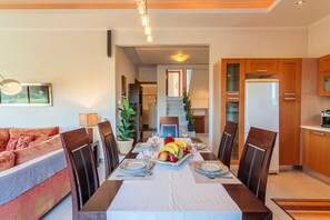 Un coin repas avec une table dressée pour quatre personnes, entouré de chaises en bois, d’un canapé et d’une cuisine en arrière-plan.