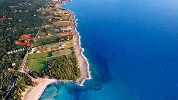 Vue aérienne d’une zone côtière avec une plage, des eaux d’un bleu limpide et une végétation luxuriante environnante.