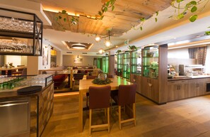 A restaurant with a wooden ceiling, hanging plants, and a bar area with glasses and plates.