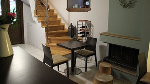 A modern living room with a wooden staircase, a fireplace, a dining table with chairs, and a wine rack. - Tsarbou Guesthouse (Gortynia)