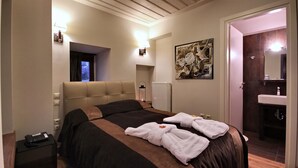A hotel room with a large bed, a bedside table with a phone, a radiator, a painting on the wall, and a bathroom with a sink and mirror. - Tsarbou Guesthouse (Gortynia)