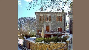 A stone building with a wooden balcony and a snow-covered exterior. - Tsarbou Guesthouse (Gortynia)