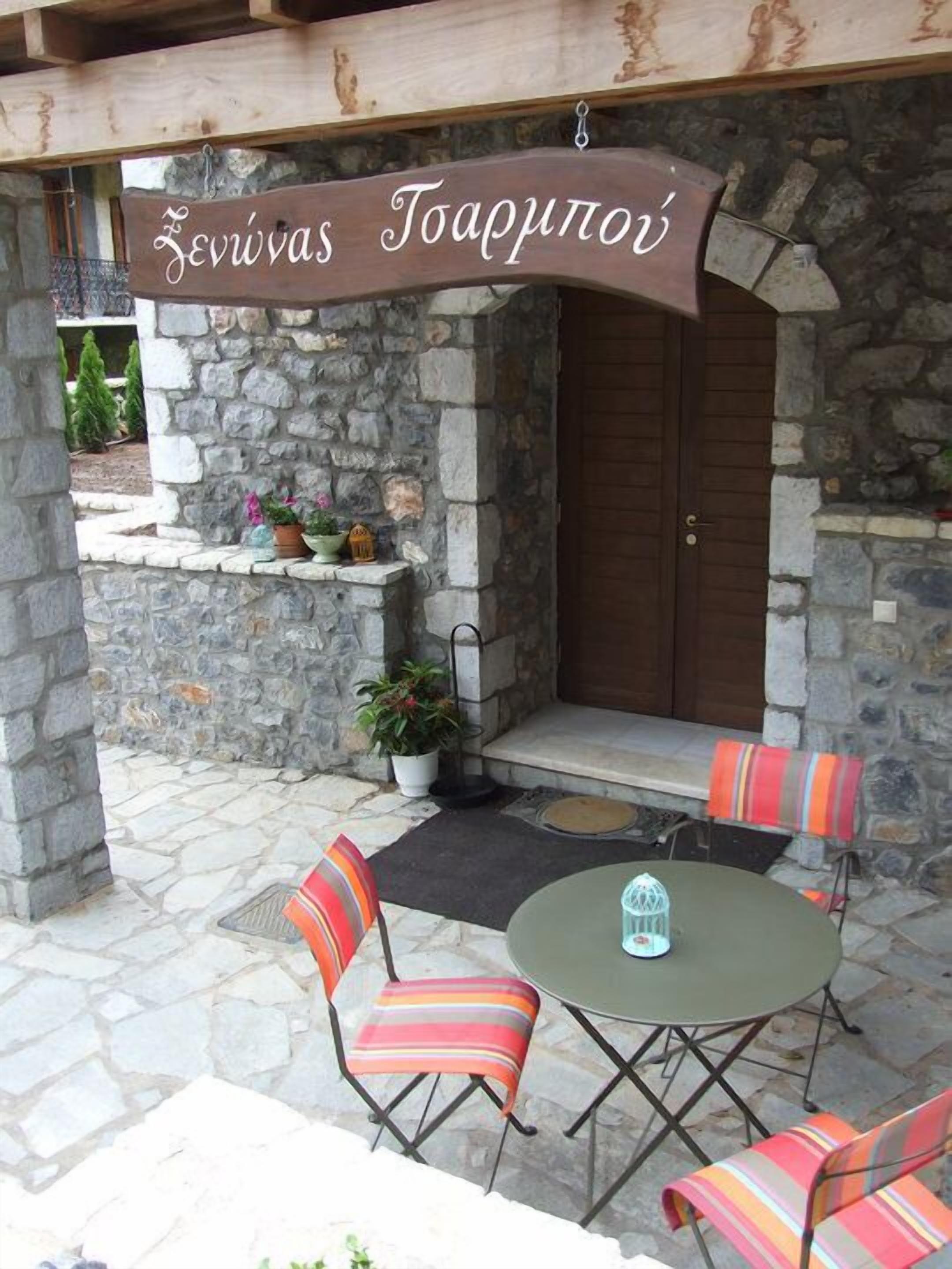 Een terras met stenen muren, een tafel, stoelen, een houten deur en een hangend bord erboven.