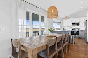 A modern kitchen with white cabinets, stainless steel appliances, and a wooden dining table. - Saltans of Swing by Brunswick Vacation Rentals: 4BR w/ Views & Across from Ocean (Holden Beach)