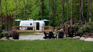 Una casa móvil con un porche cubierto y zona de estar al aire libre, rodeada de un paisaje boscoso.