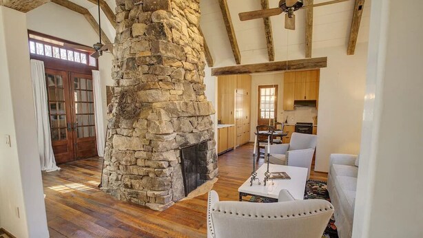 Amplia sala de estar con chimenea de piedra, vigas de madera y comedor con mesa y sillas.