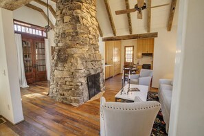 Amplia sala de estar con chimenea de piedra, vigas de madera y comedor con mesa y sillas.