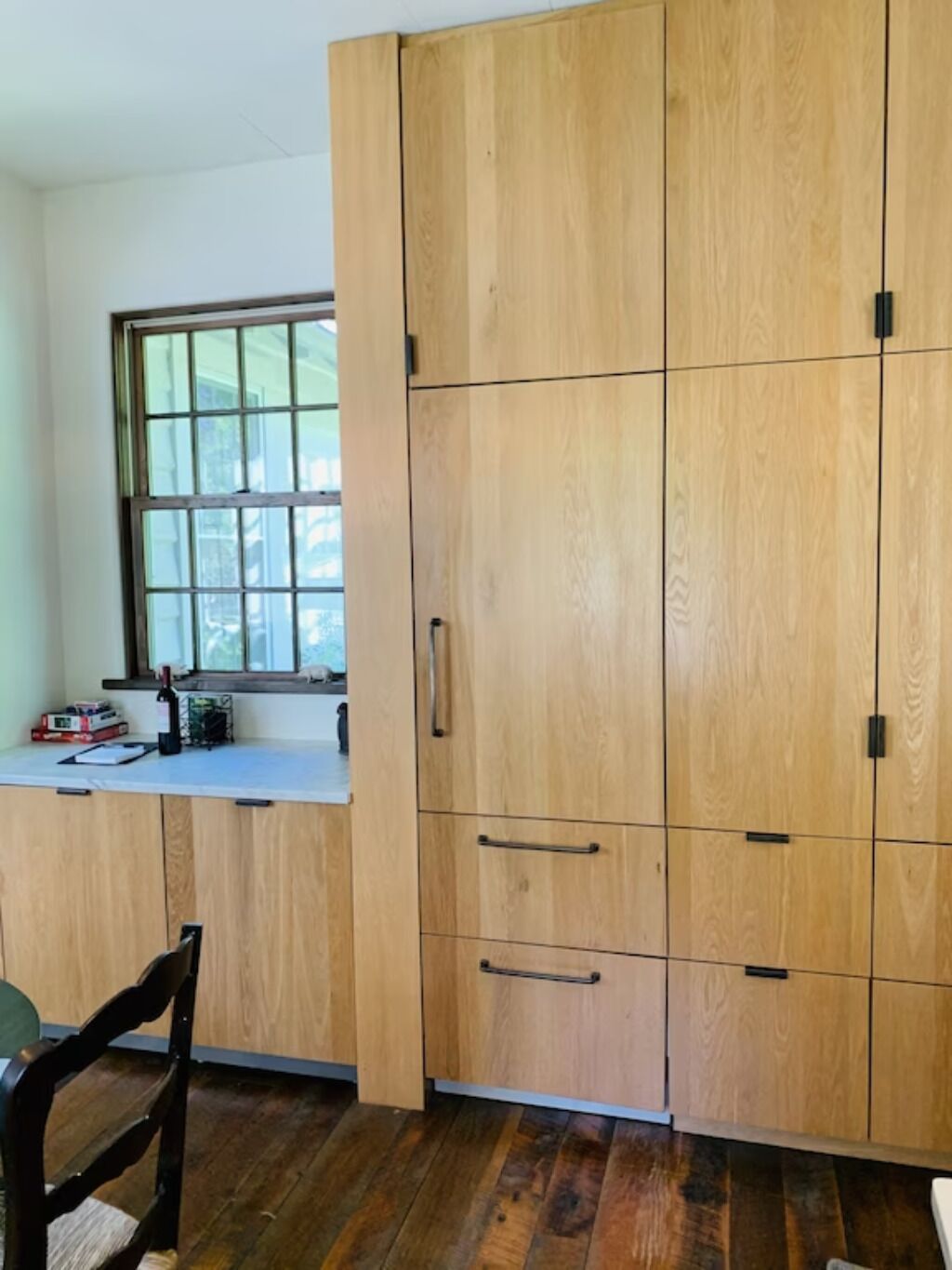 Una cocina con armarios de madera, un ventanal y un comedor con una silla.