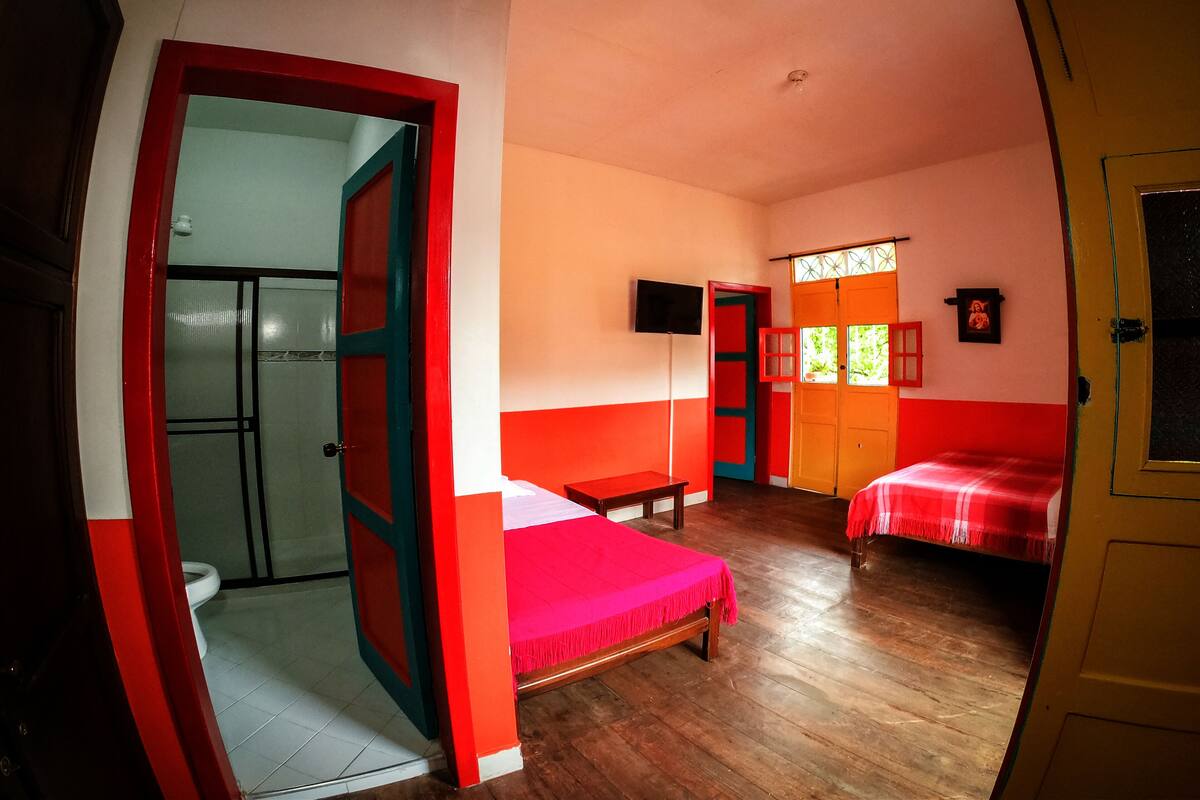 Habitación con dos camas, televisión y baño visible a través de una puerta abierta.