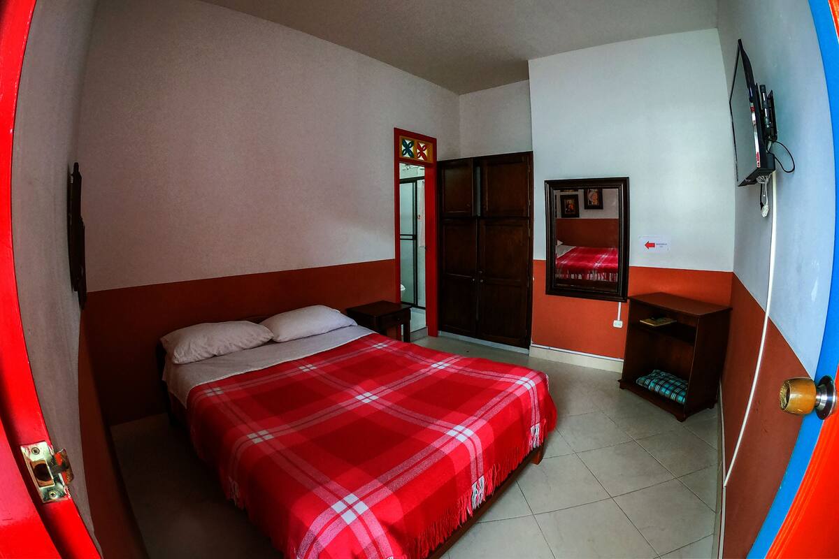 Un dormitorio con cama, armario, mesita de noche y televisor montado en la pared.