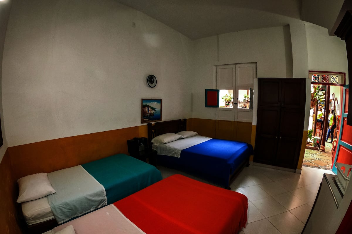 Una habitación con tres camas, un reloj, un cuadro y una ventana con vistas al exterior.
