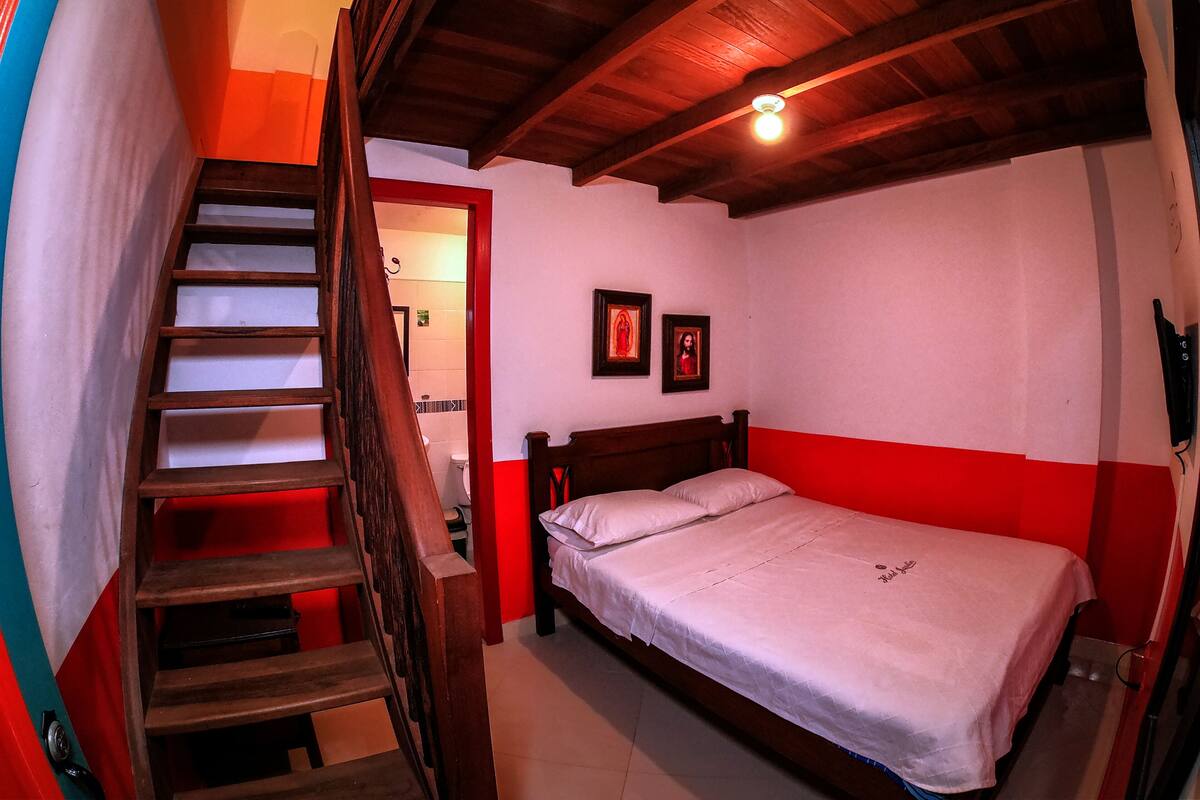Un dormitorio con escalera de madera, una cama individual, dos cuadros en la pared y una lámpara en el techo.