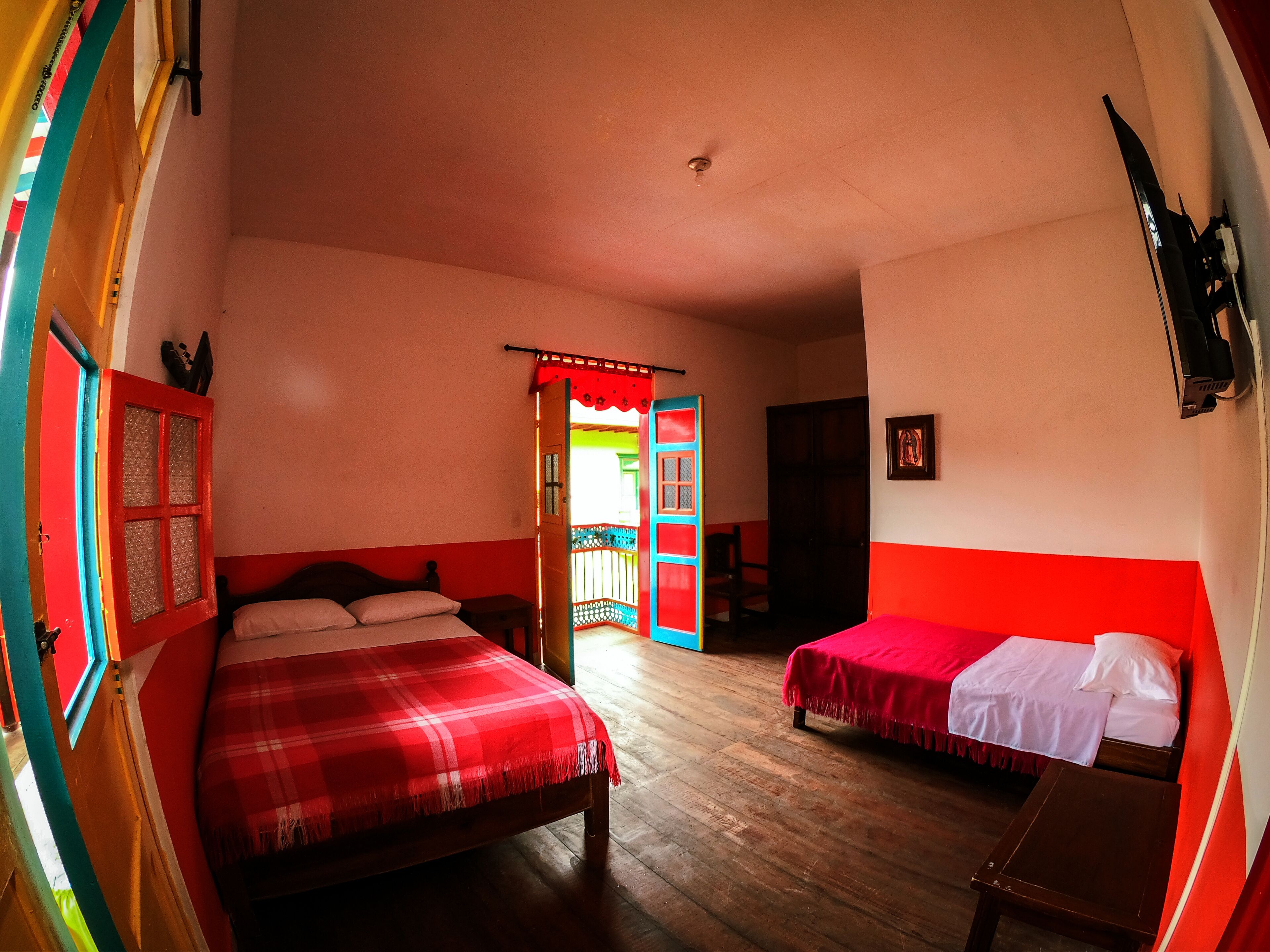 A room with two beds, a wooden floor, a red and white color scheme, and a door leading to another room.