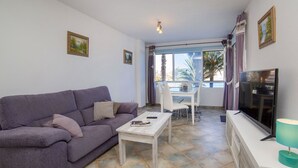 Un saló amb un sofà morat, una taula de cafè blanca i una televisió sobre un suport blanc.