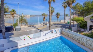 Una piscina amb vista al mar, palmeres i un paisatge urbà de fons.