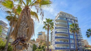 Hotel de diverses plantes amb balcons, palmeres i un cel blau clar.