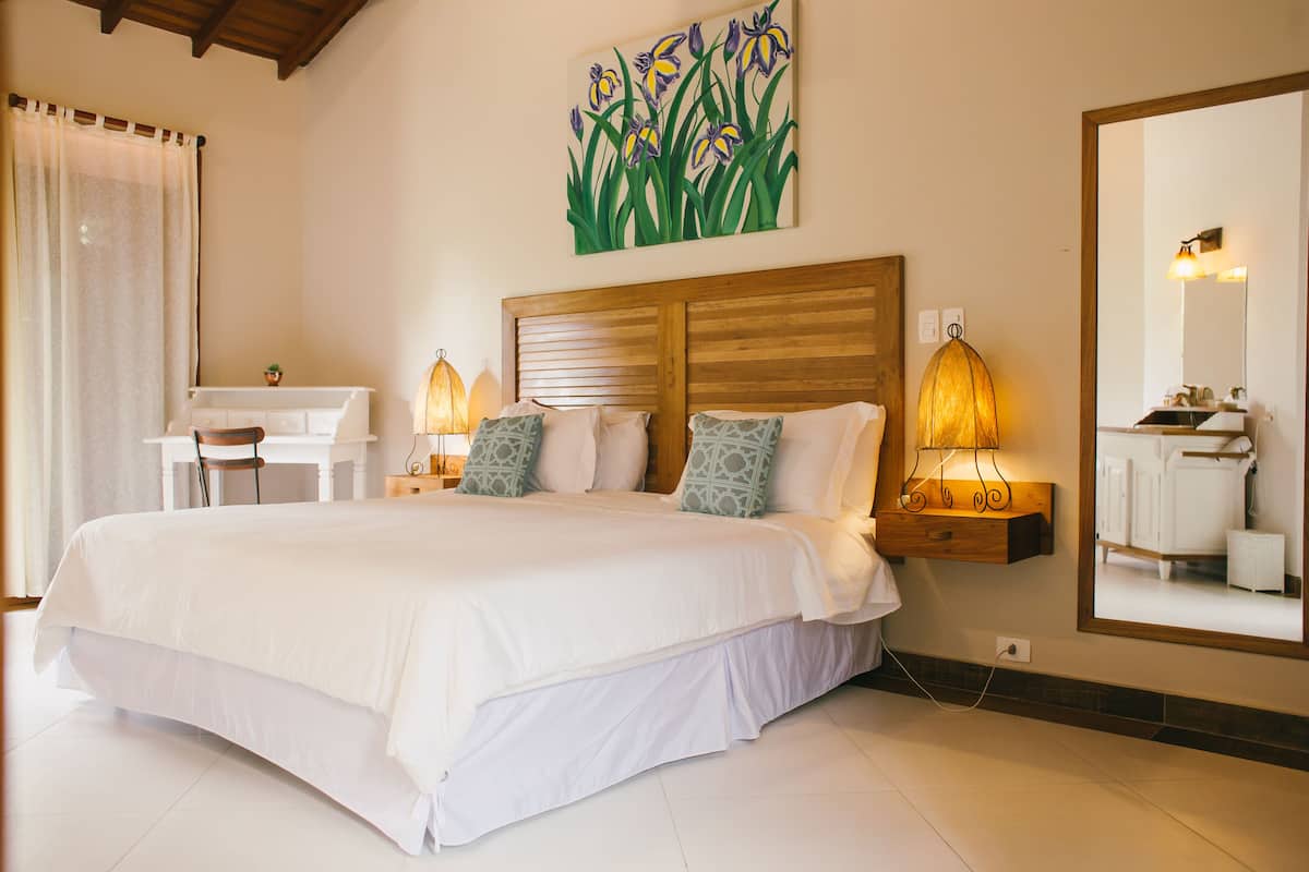 A bedroom with a large bed, bedside lamps, a desk, and a mirror.