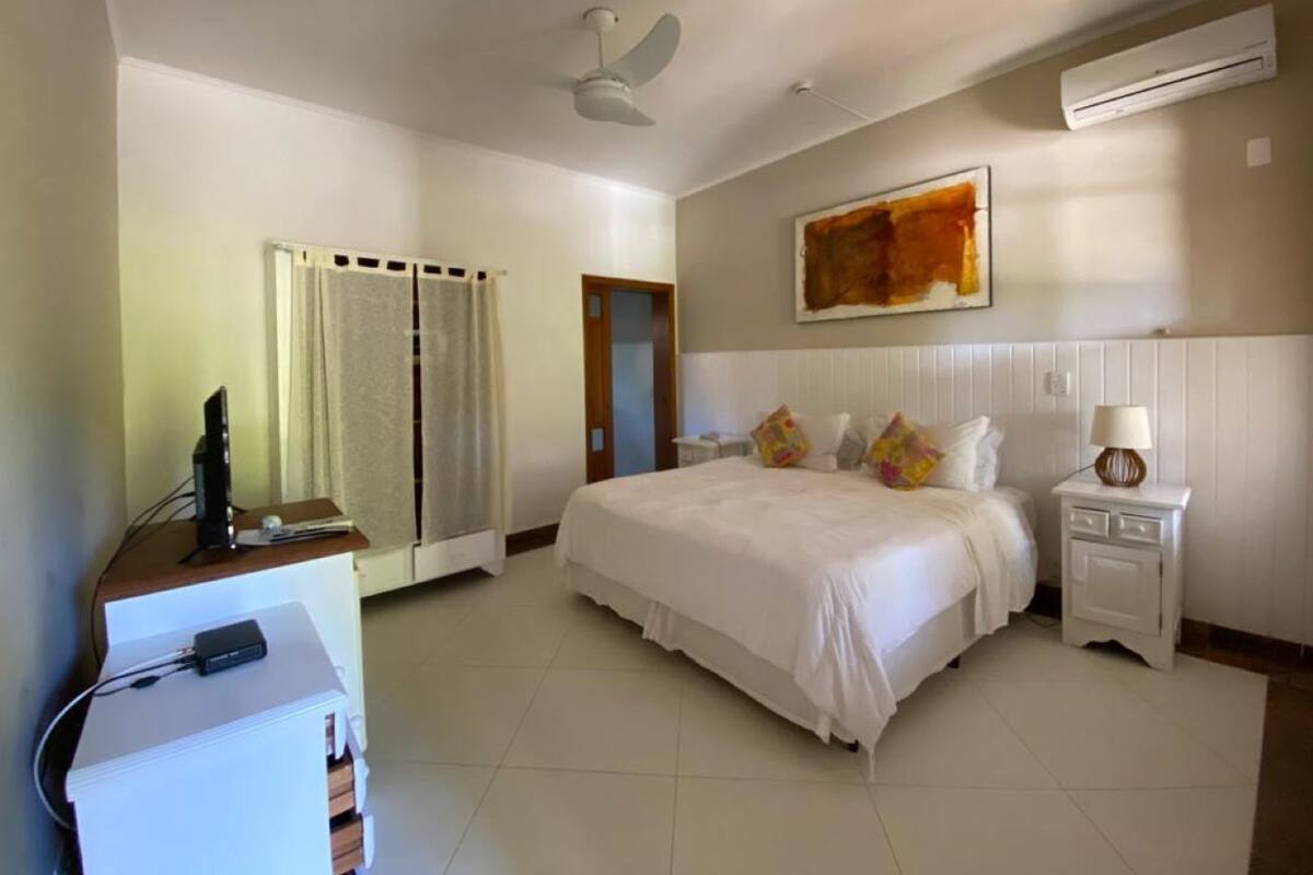 A hotel room with a bed, a desk with a computer, a nightstand with a lamp, and an air conditioning unit.
