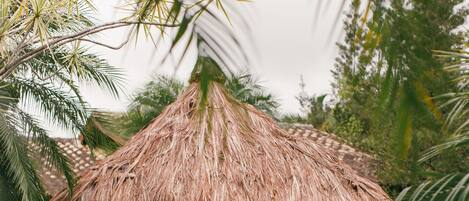 A thatched-roof gazebo with a pool in the foreground.