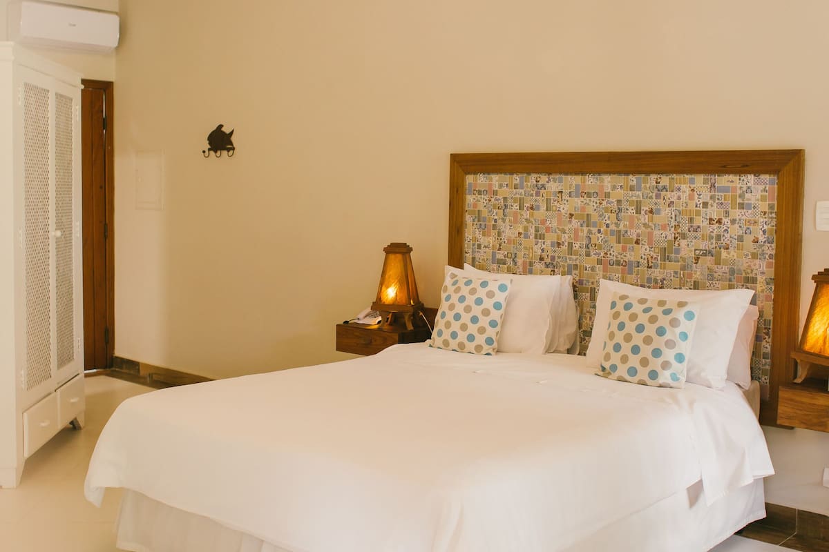A neatly made bed with white linens, a patterned headboard, and two bedside lamps.