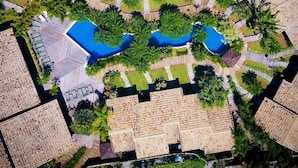Ovenudblik over en resort med flere hytter, en central pool og grønne områder.