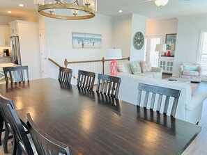 A dining area with a dark wood table and chairs, a staircase with a wooden railing, a white sofa with patterned cushions, and a wall clock.