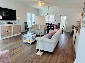 A living room with a sofa, coffee table, TV, and a dining area with chairs and a table.