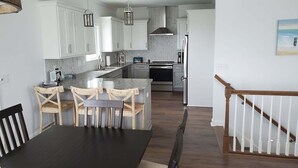 Una cucina moderna con mobili bianchi, un'isola centrale, luci a sospensione e una zona pranzo con tavolo e sedie in legno.