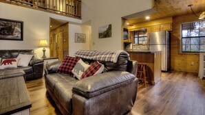 A cozy living room with a leather sofa, a wooden dining table, and a kitchen area with wooden cabinets and a refrigerator.