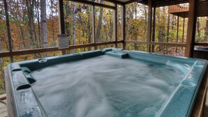 A hot tub in a wooden deck area with a view of autumn trees.