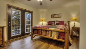 A bedroom with a wooden bed, two bedside lamps, a ceiling fan, and a door leading to a balcony.