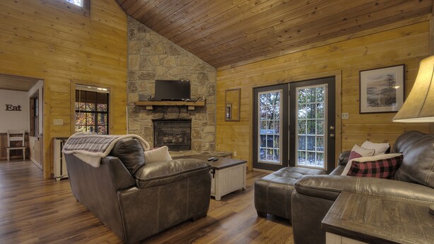 A cozy log cabin interior with a stone fireplace, leather sofas, and a dining area.