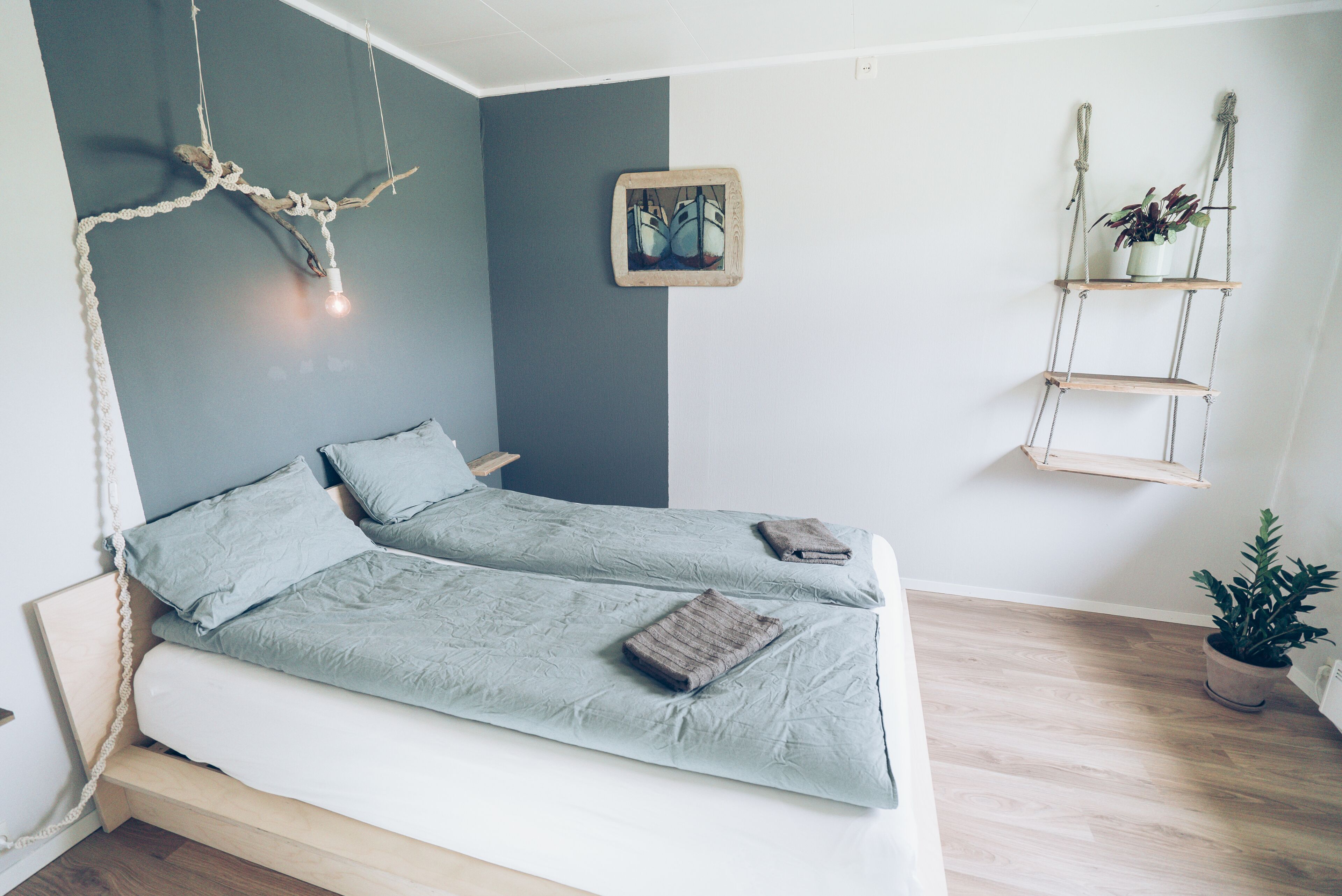 A bedroom with a bed, a hanging light, a wall-mounted shelf with a plant, and a framed picture.