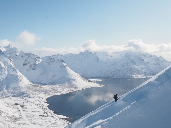 Un paysage de montagne enneigé avec un lac et une personne qui fait du ski en descendant la pente.
