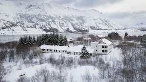 Un edificio grande de varios pisos con techo nevado, rodeado por un bosque y montañas al fondo.