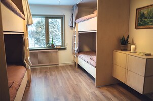 Ett studentrum med våningssängar, ett element, ett fönster med utsikt över träd, en växt, ett ljus och en tavla på väggen.