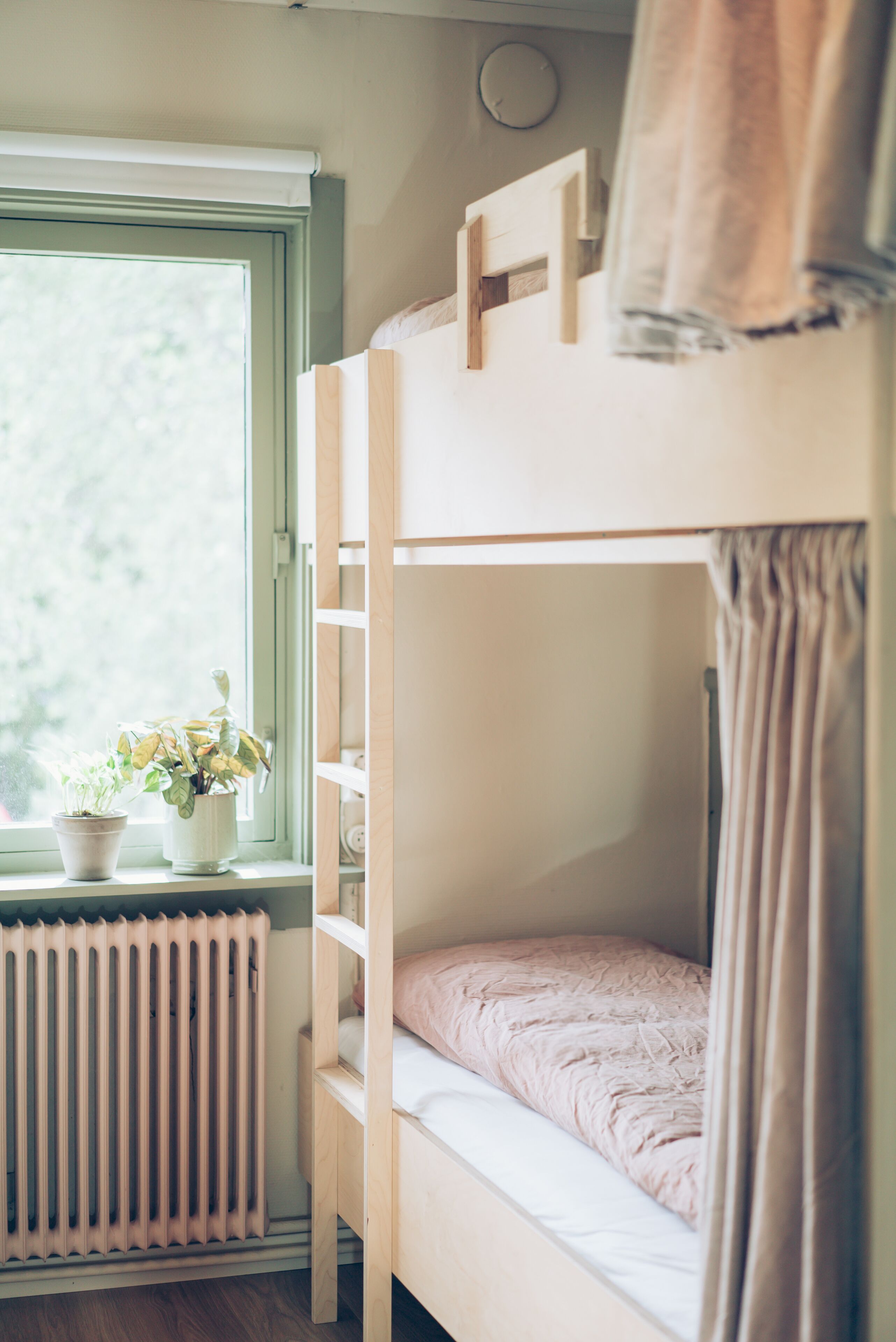 A bunk bed with a window, a radiator, and a potted plant.