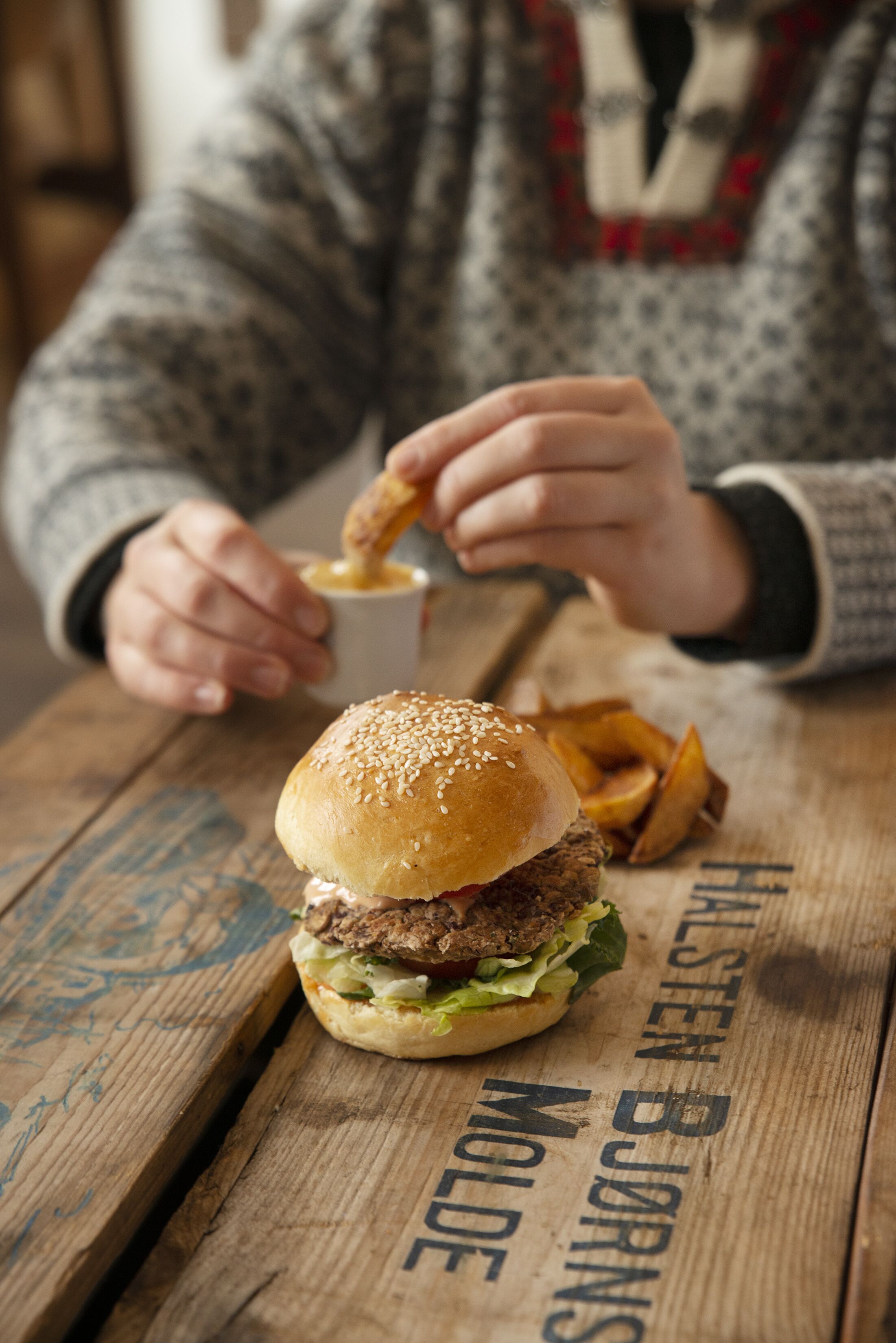 A person eating a burger and fries on a wooden table with text on it.