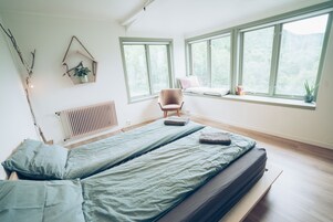 Un dormitorio con cama, sillón, ventana y radiador.
