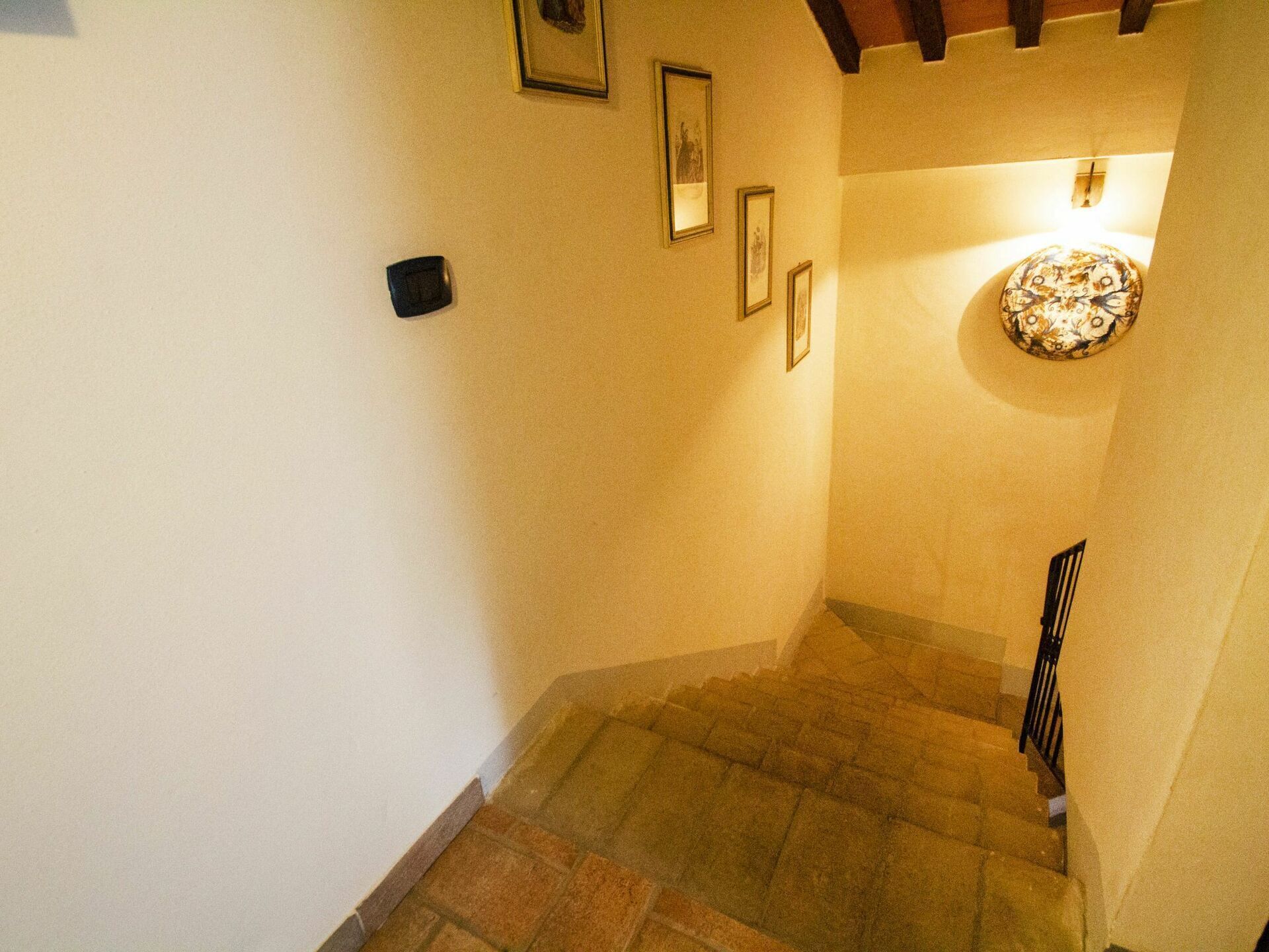 A staircase with stone steps and a wooden handrail, leading to a room with a light fixture on the wall.