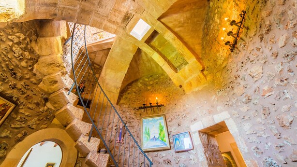 Interior de pedra com escadaria, teto em arco e obras de arte emolduradas.