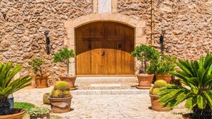 Um edifício de pedra com porta de madeira, plantas em vasos e um caminho de paralelepípedos.