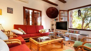 A cozy living room with a red sofa, a television, and a bookshelf filled with books. - Wonderful private villa for 8 guests with WIFI, private pool, TV and patio (Calonge)