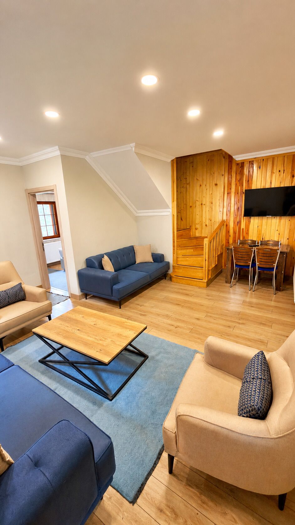 Uma sala de estar moderna com um sofá, poltronas, uma mesa de centro e uma televisão fixada numa parede de madeira.