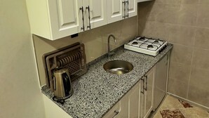 A compact kitchen with white cabinets, a stainless steel sink, and a gas stove.
